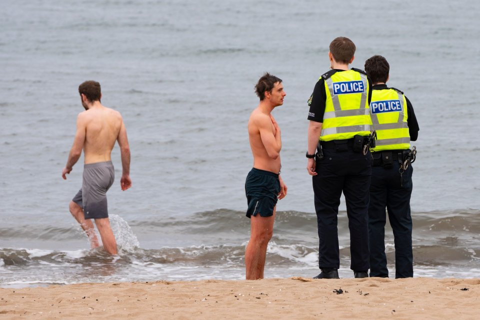  Cops talk to men wearing swimming trunks at a beach in Portobello, Edinburgh, this morning