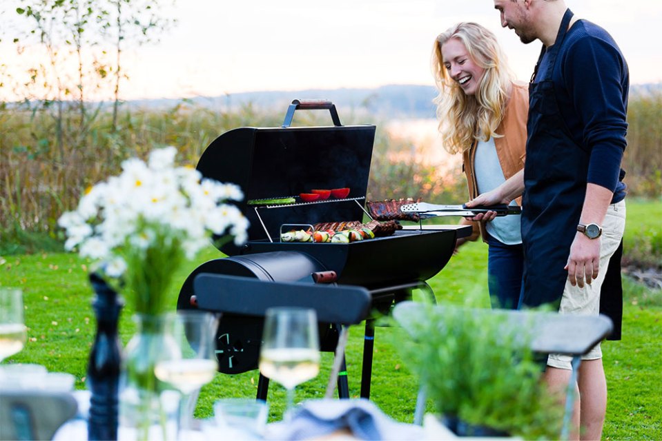 Couple grilling ribs and vegetables on a barbecue.