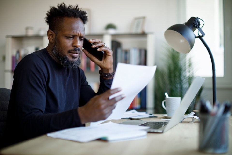 a man talking on a cell phone while holding a piece of paper