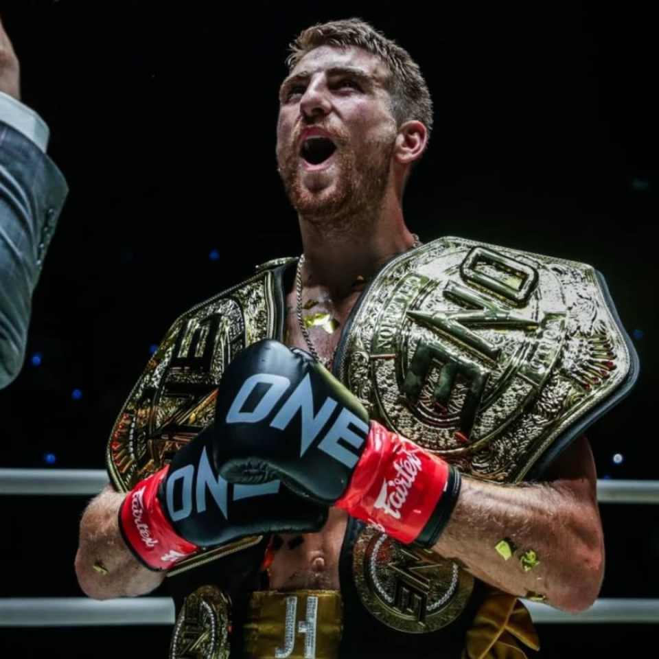 A victorious fighter holding two championship belts.