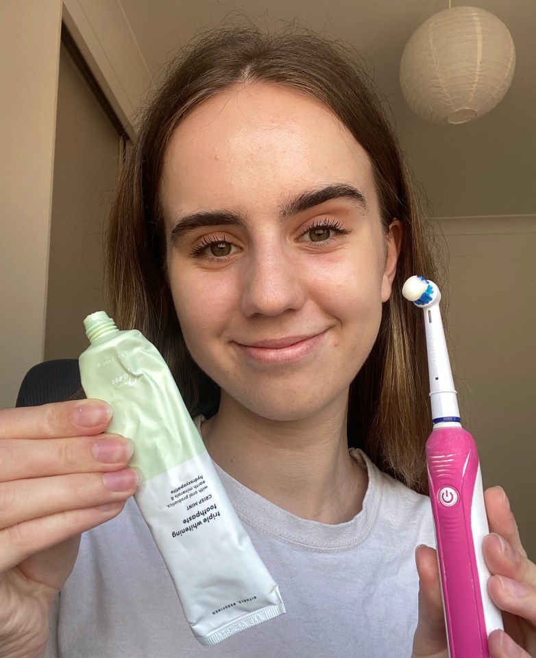 a woman holding a tube of toothpaste next to an electric toothbrush