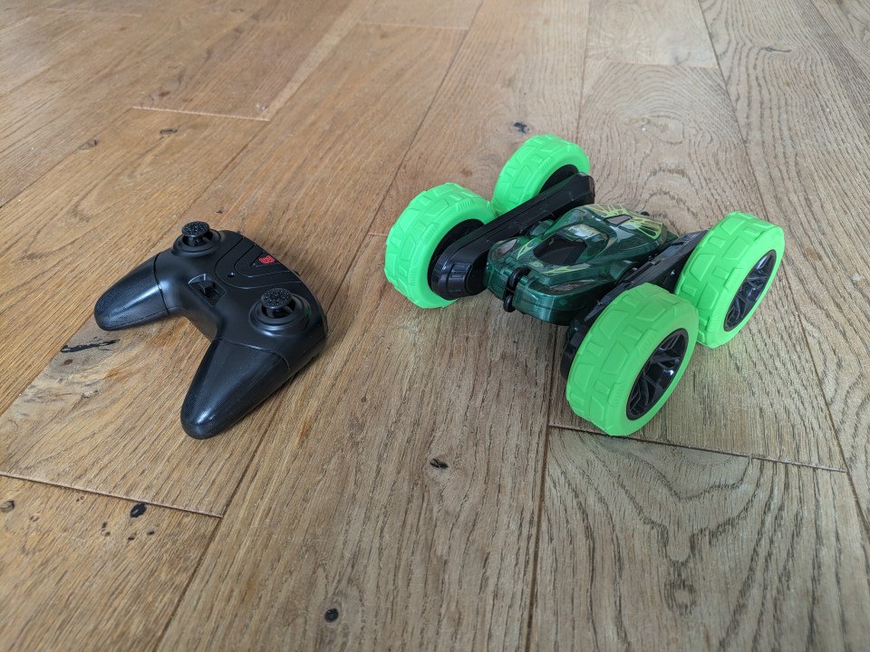 Remote control and double-sided stunt car on wood floor.