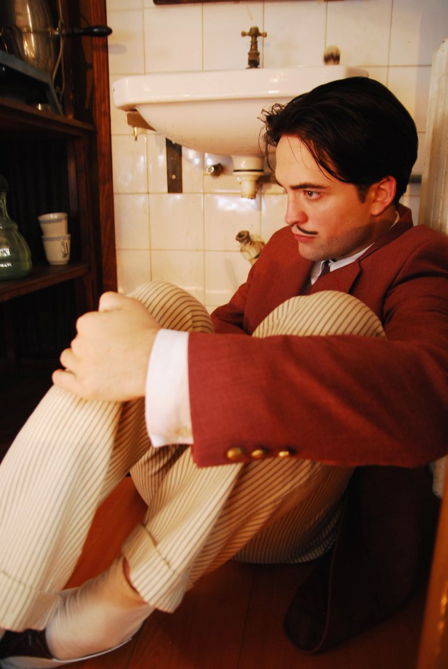 a man in a red jacket sits on the floor in front of a sink