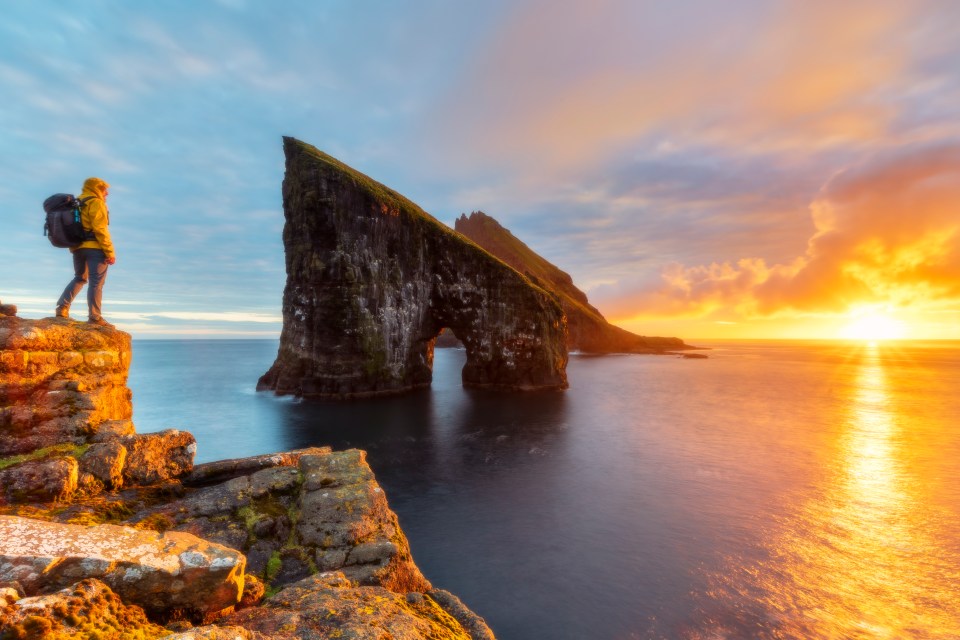 a person standing on a cliff overlooking the ocean at sunset