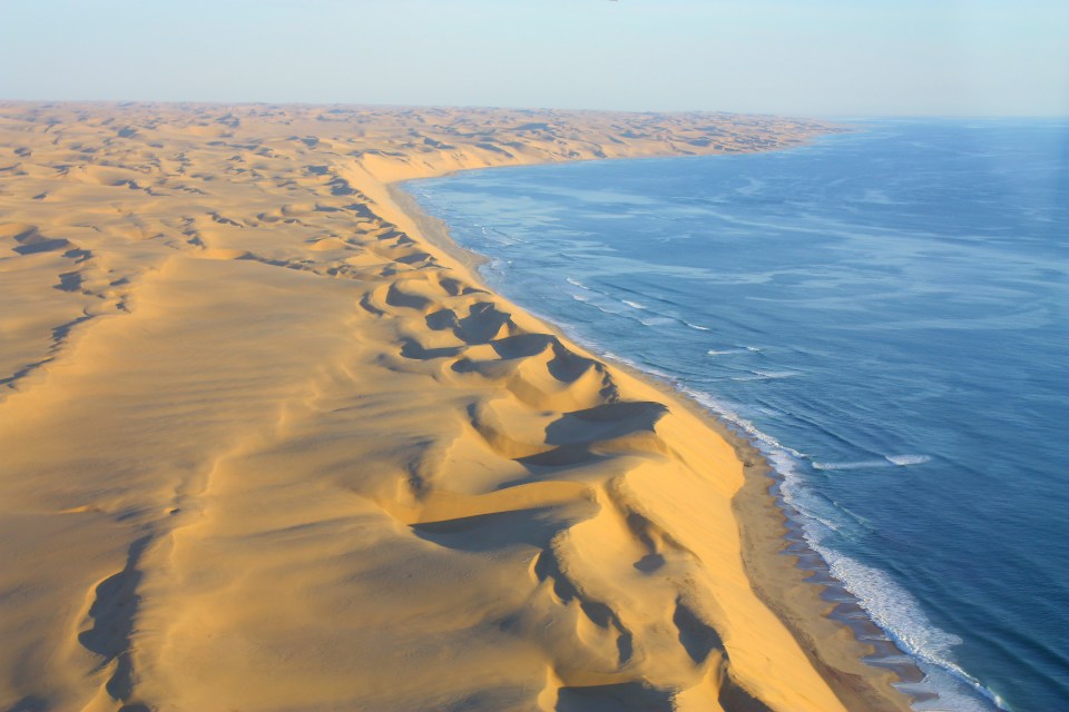 Aerial view of Namib Desert sand dunes meeting the Atlantic Ocean coastline.
