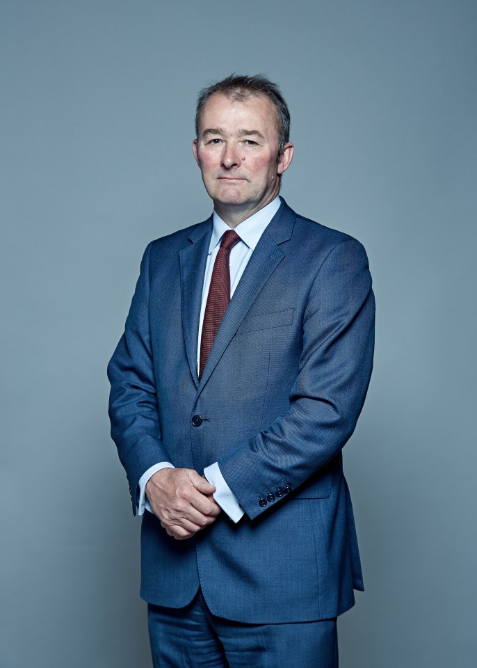 a man in a suit and tie stands with his hands folded