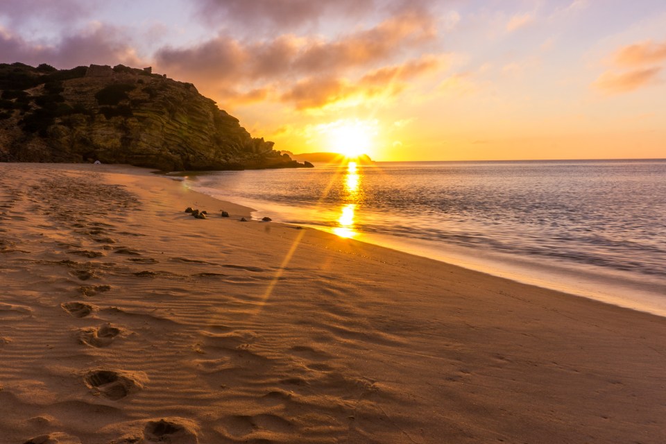 a sunset over a beach with footprints in the sand
