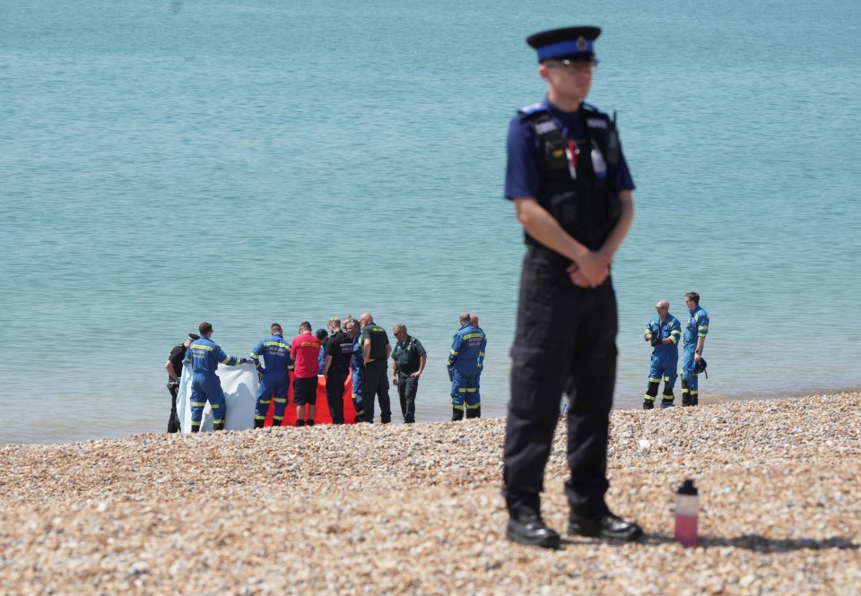 a police officer stands on the beach watching a group of people