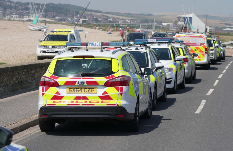 a police officer stands on the beach watching a group of people