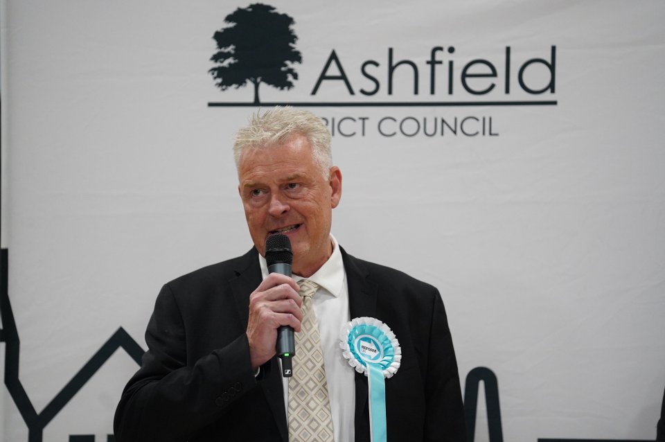 a man speaking into a microphone in front of a sign that says ashfield district council