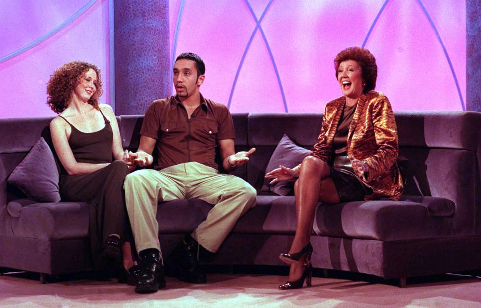 two women and a man sit on a couch in front of a purple background