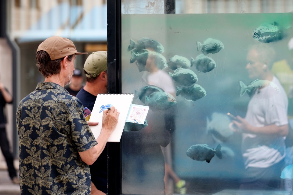 a man drawing a picture of fish on a glass wall
