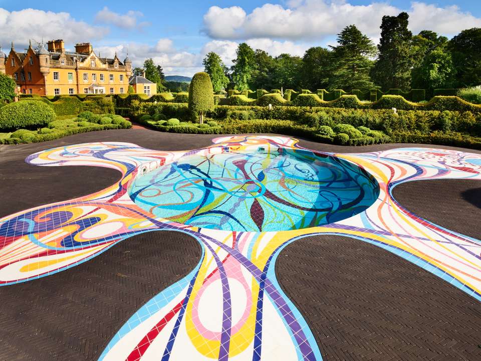 a large colorful swimming pool in a garden with a large house in the background