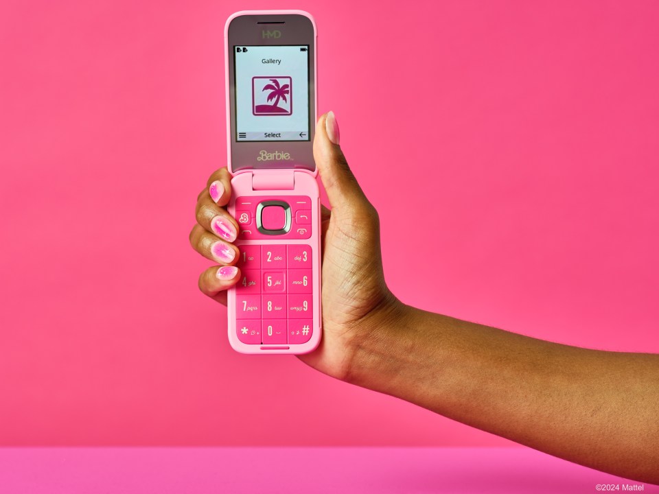 a hand holding a pink flip phone that says barbie on it