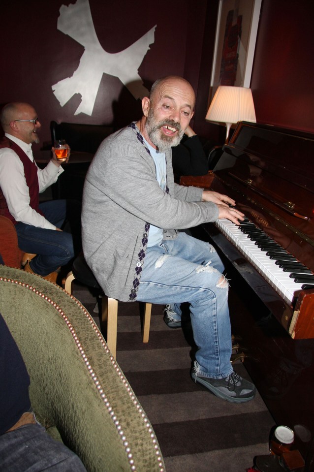 a man sits at a piano with a drink in his hand