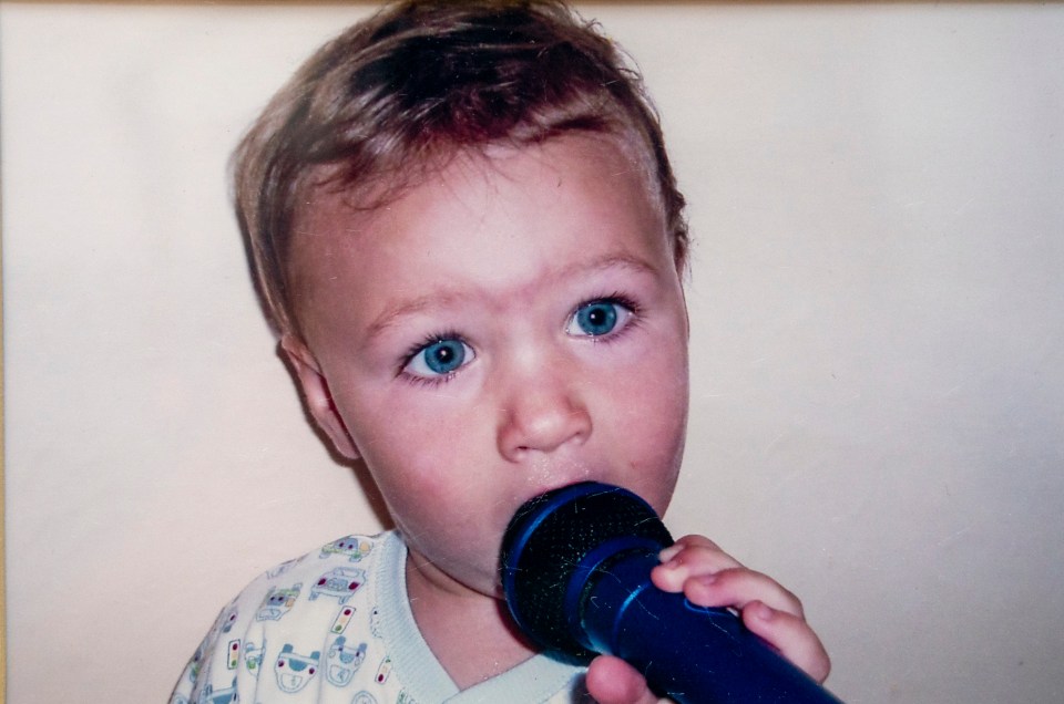 a baby with blue eyes is holding a blue flashlight in his mouth