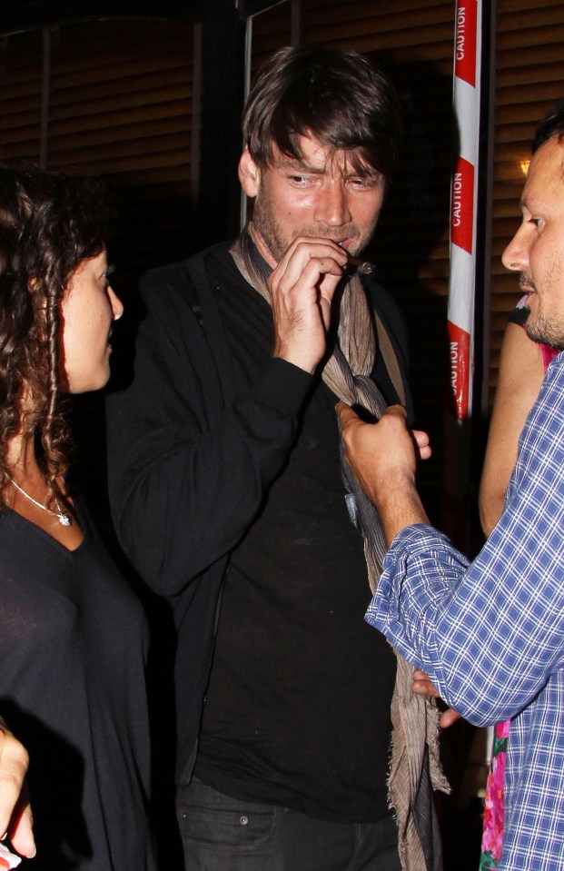 a man with a scarf around his neck is being helped by a man in a blue plaid shirt