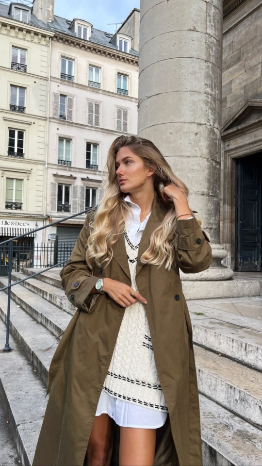 a woman in a trench coat stands in front of a building that says l' essentiel