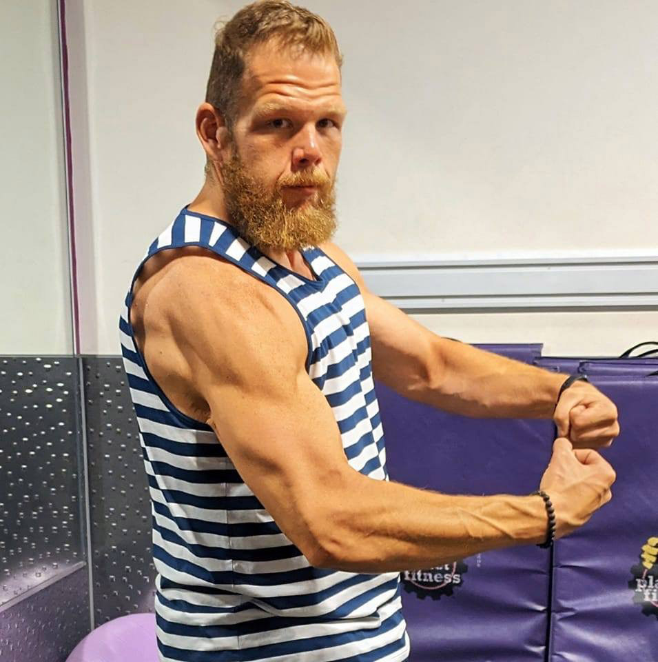 a man flexes his muscles in front of a purple mat that says fitness
