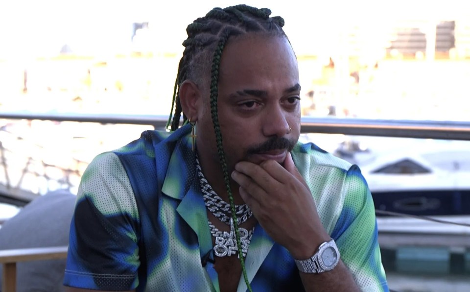 a man wearing a watch and a necklace with the letter o on it