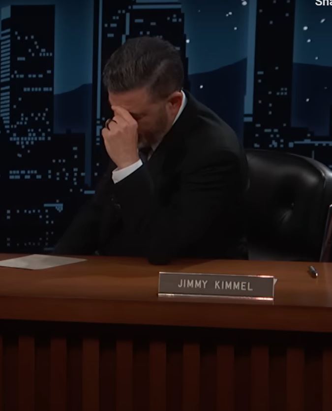 a man sits at a desk with a name plate that says jimmy kimmel