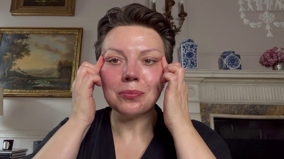 a woman is touching her face in front of a fireplace and a painting