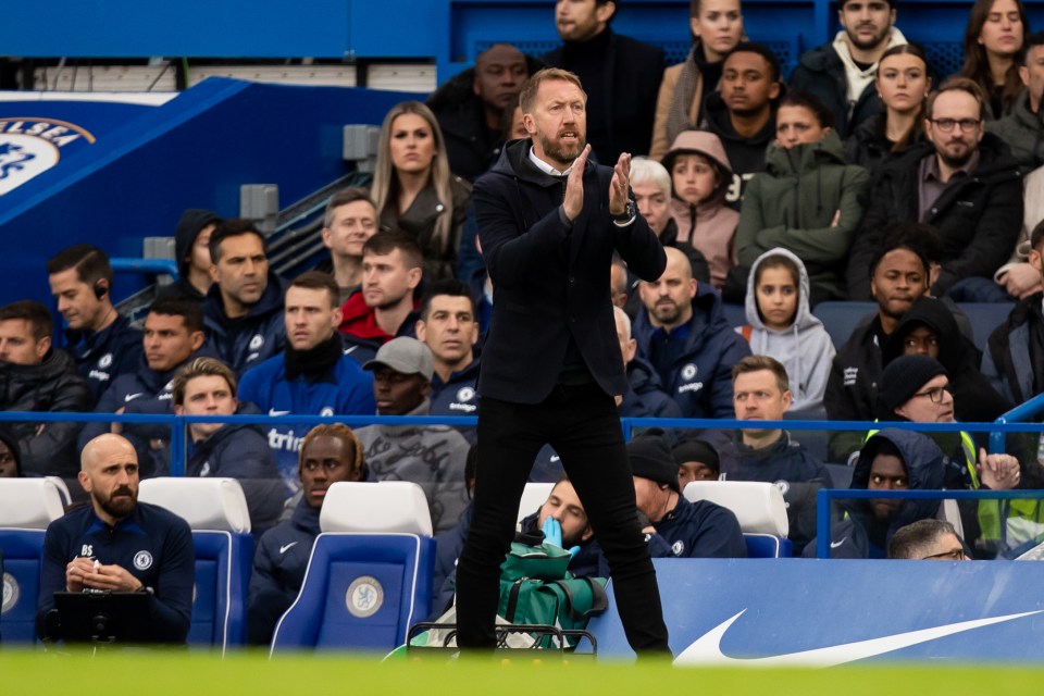 a man in a suit applauds in front of a crowd at a soccer game