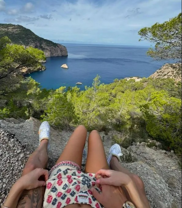 a man and a woman sit on a rock overlooking a body of water