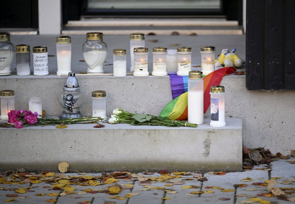 a bunch of candles are on a concrete ledge with flowers and a rainbow flag