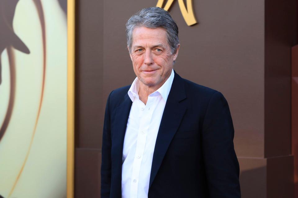 a man in a suit and white shirt stands in front of a wall with the letter n on it