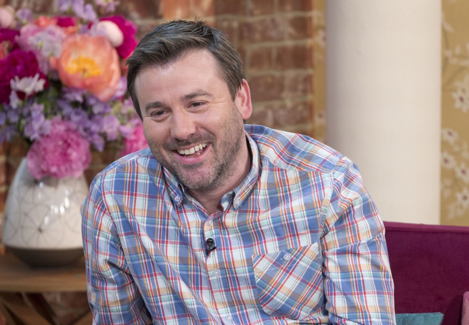 a man in a plaid shirt is smiling in front of a vase of flowers