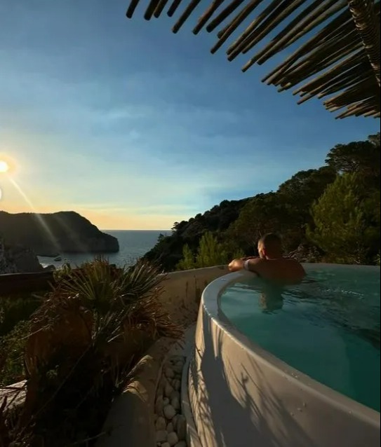 a man sits in a hot tub overlooking the ocean