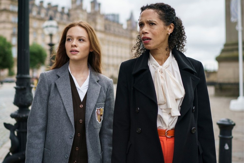 two women are walking down a street and one has a crest on her jacket