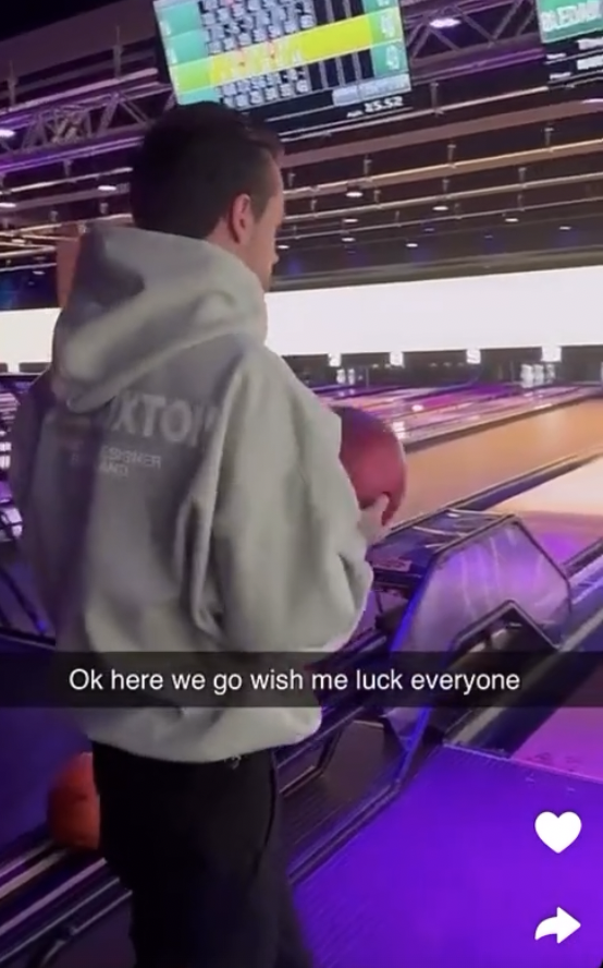 a man in a grey hoodie stands in front of a bowling alley and says ok here we go wish me luck everyone