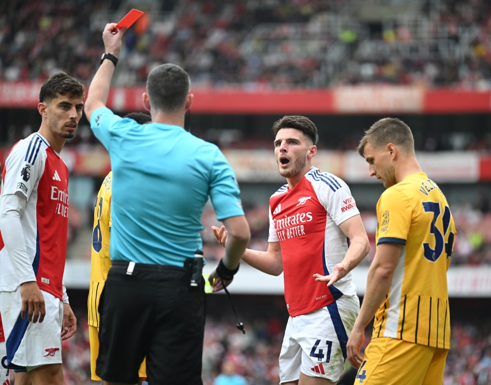 a soccer player wearing a red emirates jersey gets a red card
