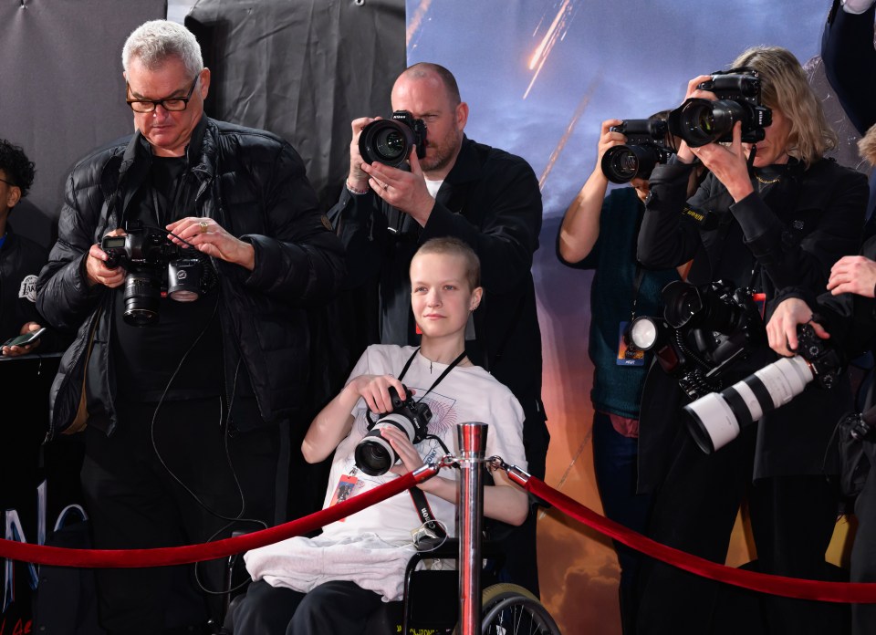 a man in a black jacket takes a picture of a woman in a wheelchair