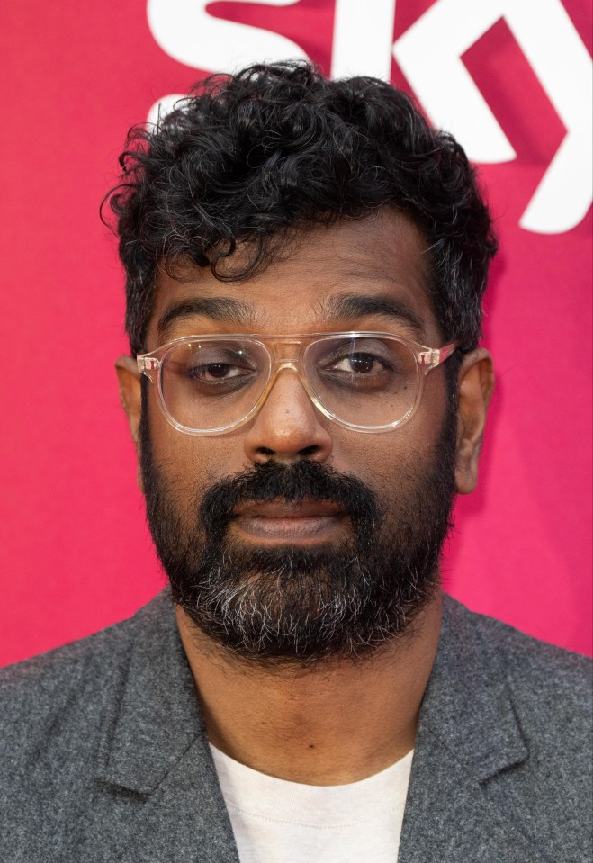 a man with glasses and a beard stands in front of a pink sky sign