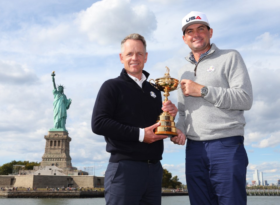 two men holding a trophy in front of the statue of liberty