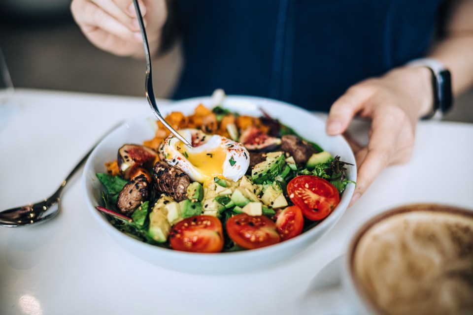a person is eating a salad with a poached egg on top