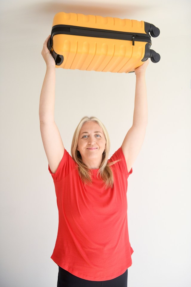a woman in a red shirt is holding a yellow suitcase over her head
