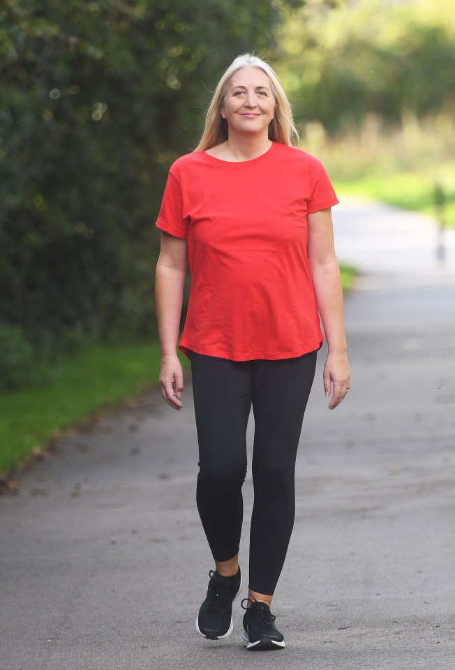 a woman in a red shirt and black leggings is walking down a road