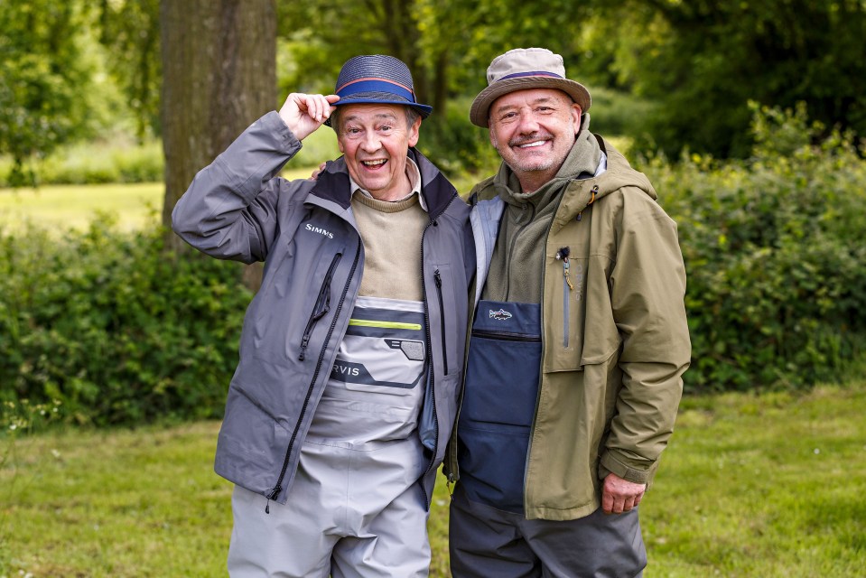 a man wearing a simms jacket stands next to another man