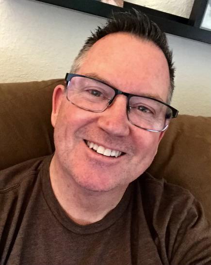 a man wearing glasses is smiling while sitting on a couch .
