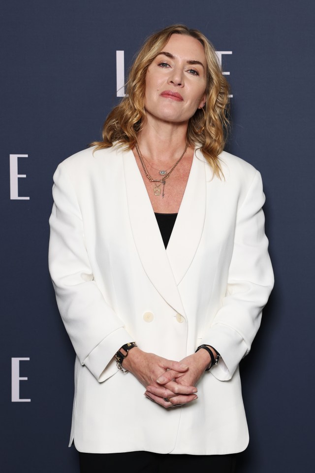 a woman in a white jacket stands in front of a blue wall with the letter e on it