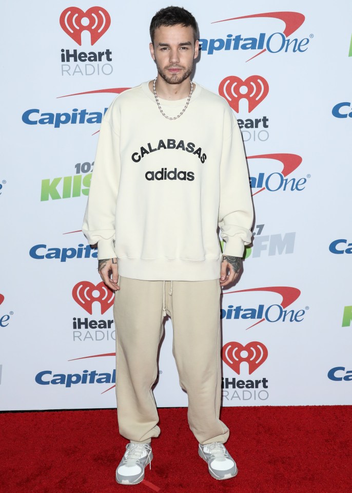 a man wearing a white adidas sweatshirt stands on a red carpet