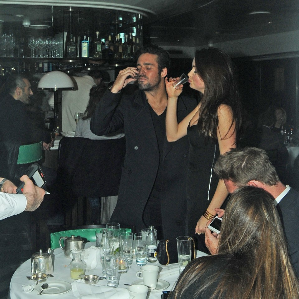 a man drinks from a glass while a woman looks on