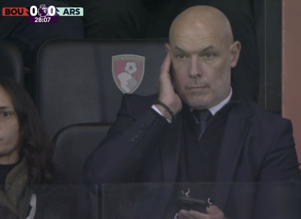 a man in a suit sits in the stands watching a soccer game