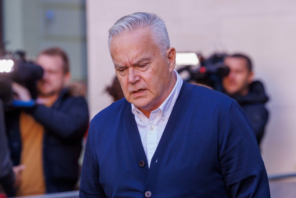 a man in a blue cardigan stands in front of a crowd of people