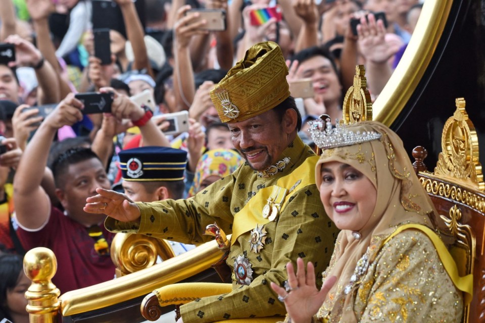 TOPSHOT - Brunei's Sultan Hassanal Bolkiah and Queen Saleha ride in a royal chariot during a procession to mark his golden jubilee of accession to the throne in Bandar Seri Begawan on October 5, 2017. Brunei's all-powerful sultan marks 50 years on the throne on October 5 with lavish celebrations including a glittering procession, a 21-gun salute and a ceremony at his vast, golden-domed palace. (Photo by Roslan RAHMAN / AFP) (Photo by ROSLAN RAHMAN/AFP via Getty Images)