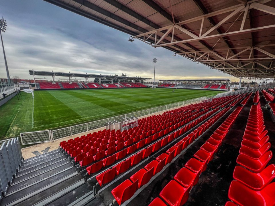 an empty soccer stadium with red seats and a green field